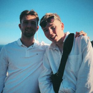 Two young men stand on a bridge and pose together.