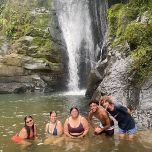 Group of five students stands in a waterfall basin.