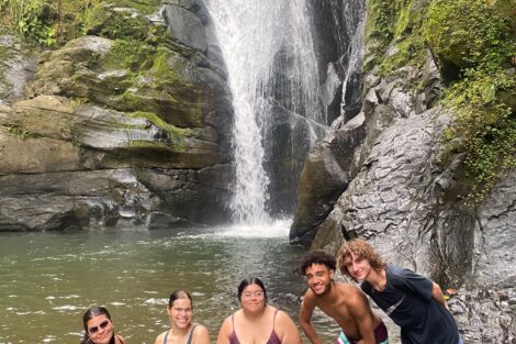 Group of five students stands in a waterfall basin.