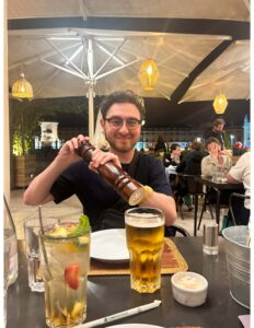 Jacob Ingwer, a young white man with brown hair and glasses, sits at a restaurant table in Copenhagen while holding a pepper grinder.