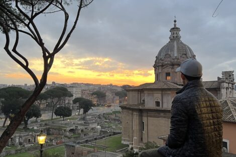 A man sitting on a ledge overlooking a city skyline with a large domed building in the background.