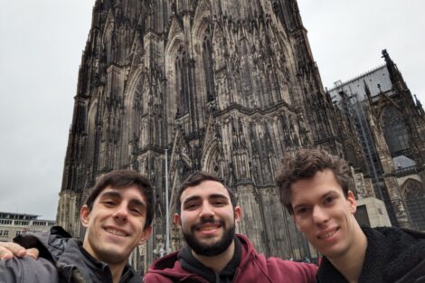 Three young men stand in front of a chapel in Germany.