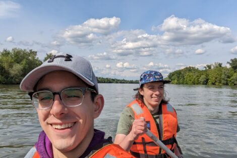 Two men wearing life vests in a kayak on a wide river.