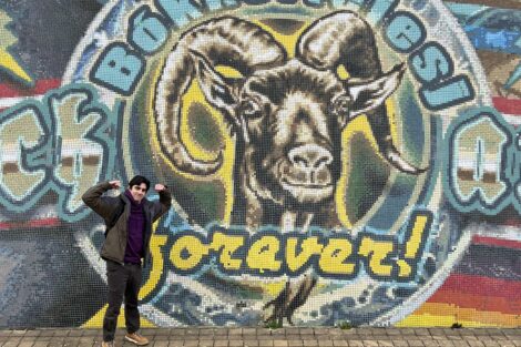 A man standing in front of a wall with a large mural of a ram that says 