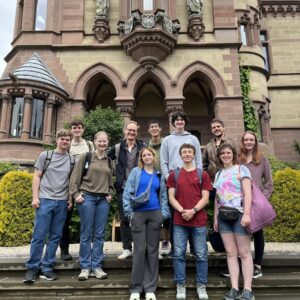 Group of 11 people standing on the steps outside a stone building with decorative statues of religious figures.