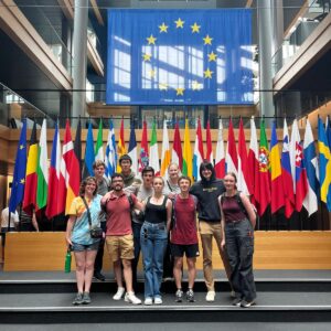 Group of 10 students standing in front of a row of international flags at the United Nations.