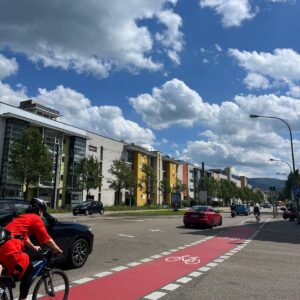 Street in a German town. A cyclist is riding through the red bike lane and there are a few cars in the street.